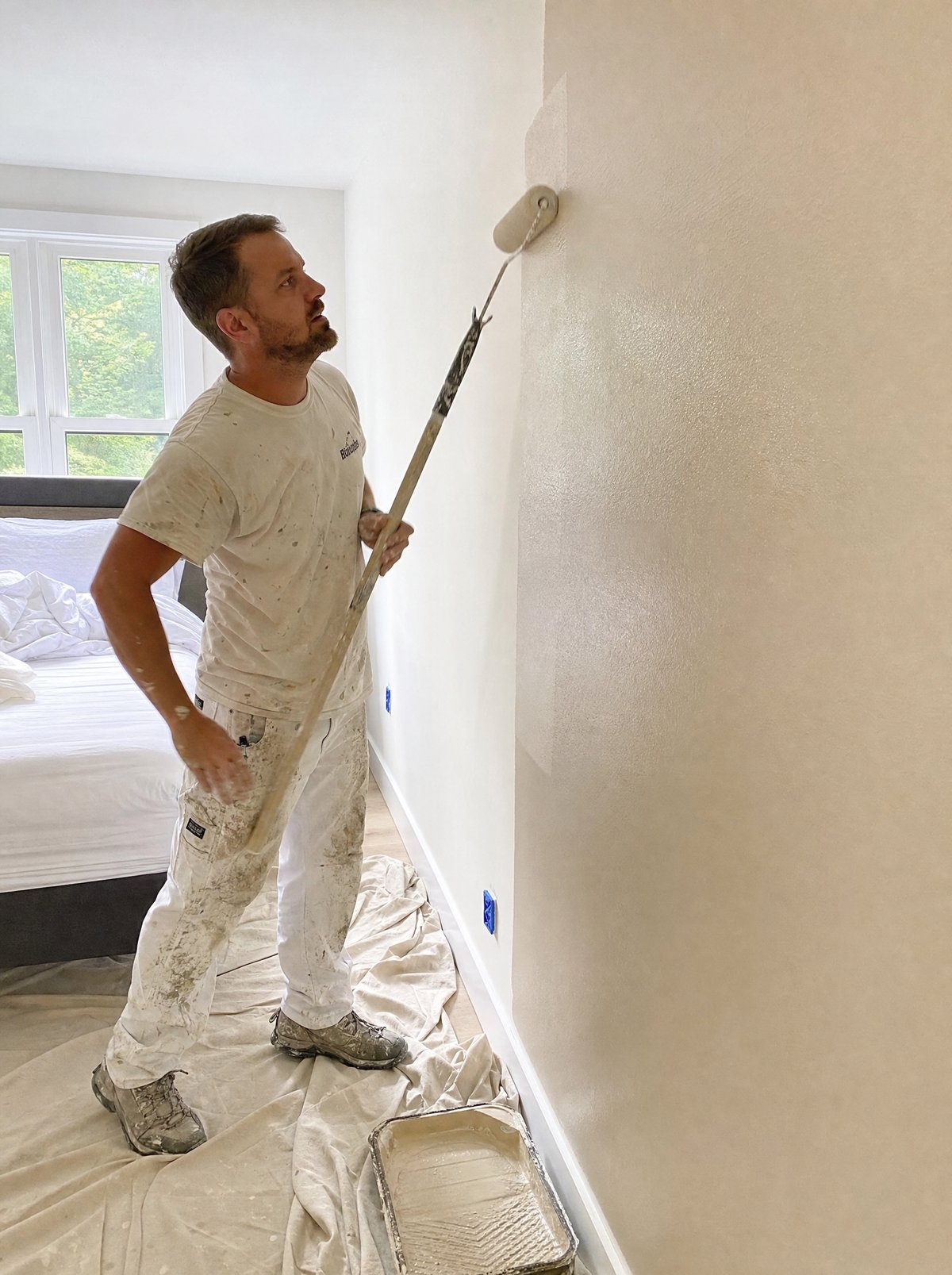 A painter rolling fresh paint onto a bedroom wall