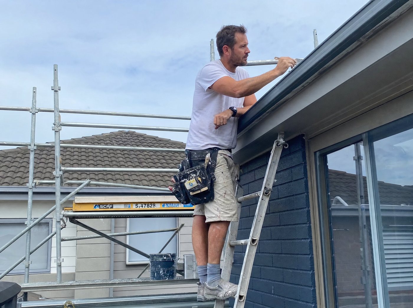 A roofer working on a house exterior from a ladder