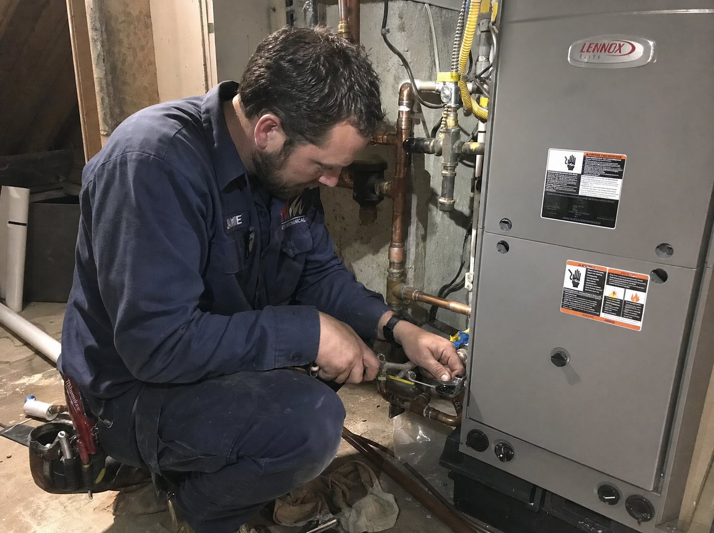 An HVAC technician servicing a furnace and copper pipes in a basement