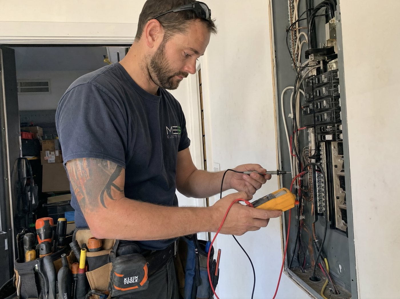 A licensed electrician working at an open electrical panel